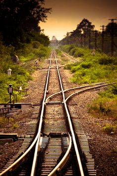 an old train track with the sun setting in the background and trees on both sides