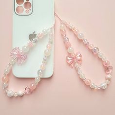 an iphone case with a pink bow and pearls on it next to a phone chain