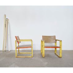 two wooden chairs sitting next to each other on cement floored area with white wall in background