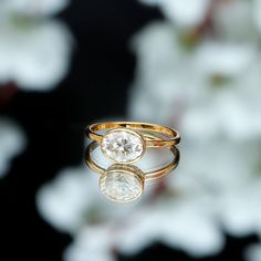 two gold rings sitting on top of each other with a diamond in the middle and white flowers behind them