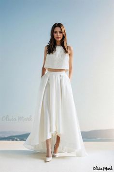 a woman standing on top of a beach wearing a white skirt and cropped top