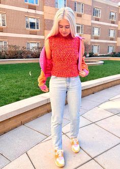 a woman standing in front of a brick building wearing jeans and a sweater with an open back