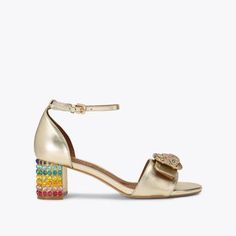 The Mayfair Block Mid Heel features a metallic gold upper in soft suede. The open toe is accented with oversized antiqued brass buckle with crystal eagle head and surrounding crystals. Heel height: 1.9inRainbow crystal embellishment on the block heelPadded and quilted footbedMaterial: LeatherStyle number: 9990561109 Embellished Gold Leather Sandals, Gold Embellished Leather Sandals, Luxury Gold Heels With Stacked Heel, Luxury Gold Stacked Heel, Gold Low Heel Sandals With Buckle Closure, Gold Leather Heels With Rhinestones, Gold Leather Sandals With Rhinestones, Gold Embellished Low Heel Shoes, Gold Embellished Low Heel Heels