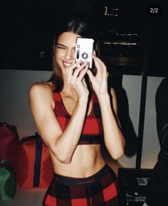 a woman taking a selfie with her cell phone while wearing a plaid skirt and crop top