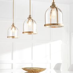 three pendant lights hanging over a table in a white room with a bowl on it