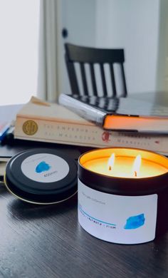 a candle sitting on top of a wooden table next to a book and laptop computer