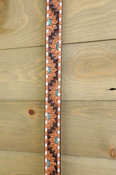 a brown and blue flowered belt on wooden planks next to a wall with wood boards in the background