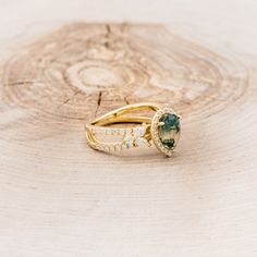 two gold rings with green and white stones sitting on top of a tree stump in the woods