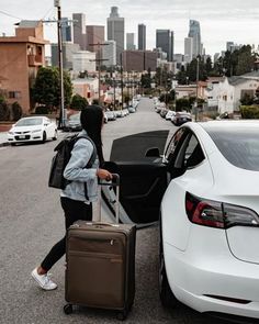 a woman is pulling her suitcase out of the back door of a white car on a city street