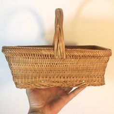 a hand holding a wicker basket in front of a white wall