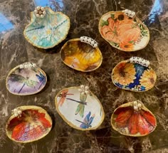 six decorative dishes with dragonflies and flowers painted on them sitting on a marble surface