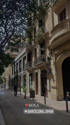 an empty street with people walking on the sidewalk and trees in front of buildings that have balconies