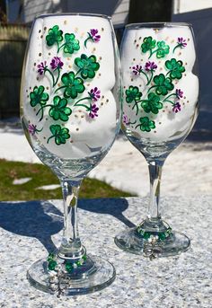 two wine glasses with green and purple flowers painted on the glass are sitting next to each other