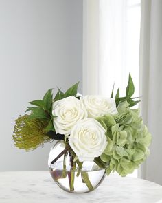 a vase filled with white flowers and greenery on a table next to a window