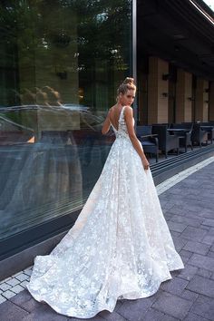 a woman in a white wedding dress standing on the side of a building with her back to the camera