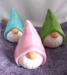 three small ceramic gnomes sitting on top of a purple tablecloth covered table cloth