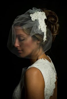 a woman with a veil on her head wearing a white dress and hair comb in front of a black background