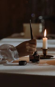 a person writing on a piece of paper with a candle in front of them at a dinner table