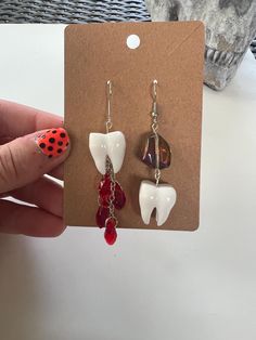 This listing is for one pair of white tooth dentist gemstone sparkle halloween dangle earrings. Comes in either the red crystal blood drop OR the gray gemstone variety. NOT A REAL TOOTH Hand made with UV resin and accessories. Earrings hooks are hypoallergenic and fully customizable in silver or gold color. Just leave a note at checkout of which you prefer if your preference is not shown in the photo!  Super lightweight, cute, spooky earrings that have a classy gothic vibe- perfect for Halloween! Due to the handmade nature of these earrings, there may be slight color/shape variations or imperfections, but the creepy & cute vibe will be in every pair.  Customizations for all earrings are OPEN, just message me to craft your perfect pair. IG: @cutecreepybymacenzie Teeth Earrings, Oddities And Curiosities, Tooth Earrings, Spooky Earrings, Teeth Dentist, Blood Drop, Gray Gemstones, Earrings Gothic, Earrings Halloween