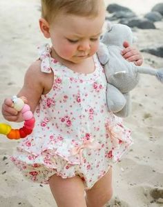 a baby girl walking on the beach with a stuffed animal in her hand and sand behind her