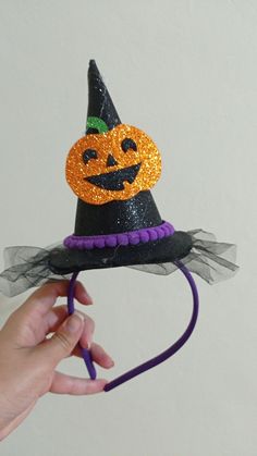 a hand holding a halloween hat with a pumpkin on it