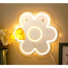 a flower shaped light up mirror on the wall next to a vase with flowers in it