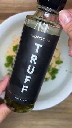 a person holding a bottle of truffle oil in front of a white plate