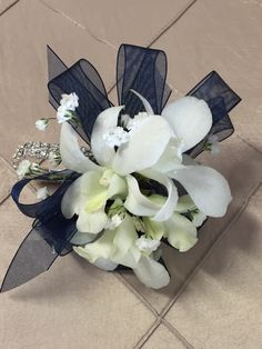 a bridal bouquet with white flowers and blue ribbon on the floor in front of a tiled floor