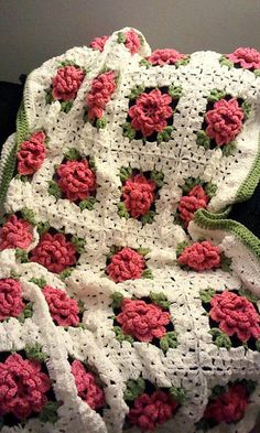 a crocheted blanket with pink flowers on it is sitting on a black chair