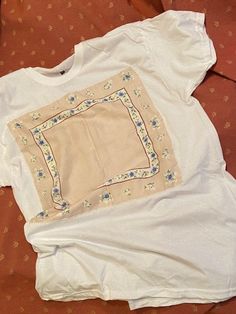 a white t - shirt laying on top of a bed next to an orange pillow