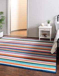 a room with a bed, table and colorful rugs on the floor in front of it