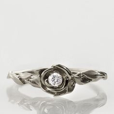 a white gold ring with a diamond in the center and leaves on it's sides