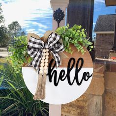 a wooden sign with the word hello written on it and a bow hanging from it