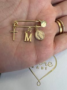 a person's hand holding two gold rings with the letter m and a coin