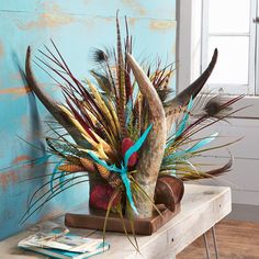 a vase filled with lots of different colored feathers on top of a wooden table next to a blue wall