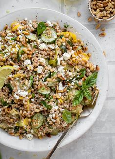 a white bowl filled with rice and vegetables next to two bowls of nuts, lemon wedges and lime