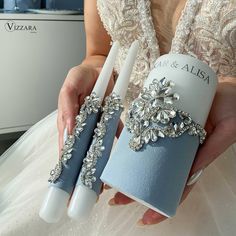 a woman holding two blue and white wedding garters with crystal brooches on them