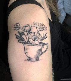 a black and white photo of a flower in a cup tattoo on the left arm