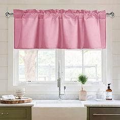 a kitchen sink under a pink curtain in front of a window