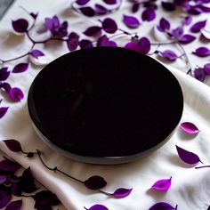 a black bowl sitting on top of a white cloth covered in purple flowers and leaves