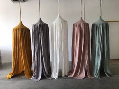 four different colored drapes hanging from hooks in an empty room with concrete flooring