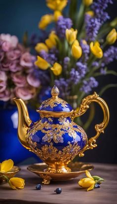 a blue and gold tea pot sitting on top of a table next to yellow flowers