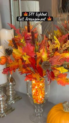 a vase filled with lots of fall leaves and candy corn sitting on top of a table