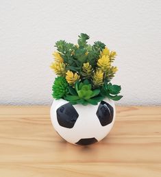 a soccer ball vase with plants in it on a wooden table next to a white wall