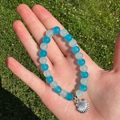 This Is A Handmade Light Blue And Aqua Glass Beaded Bracelet. This Bracelet Is Colorful And Very Pretty. This Would Be A Nice Addition To Almost Any Outfit. It Has A Seashell Charm On It. This Bracelet Is Fitted And Won't Move Around Much When You Are Wearing It. Handmade, Causal, Beachy, Beach Themed, Ocean, Shell, Sea Shell, Sea Shell Charm, Beachcore, Feminine, Girly, Light Aqua Blue, Light Blue, Aqua Blue, Aqua, Coastal Coastal Blue Beaded Jewelry, Blue Beaded Beachy Jewelry, Handmade Blue Jewelry For Beach Season, Adjustable Blue Beachy Jewelry, Blue Adjustable Beachy Jewelry, Blue Beaded Hand-strung Bracelets For The Beach, Beachy Blue Adjustable Jewelry, Blue Hand-strung Jewelry For Summer, Blue Beachy Jewelry For Vacation