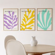 three framed art prints on the wall above a dining room table with chairs and vase