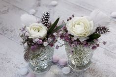 two glass vases with flowers and feathers on the table next to eggshells