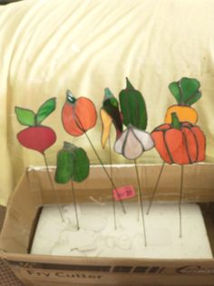 a cardboard box filled with fake vegetables on top of a bed next to a pillow