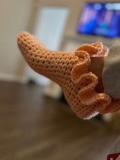 a persons hand holding a pair of knitted slippers in front of a television