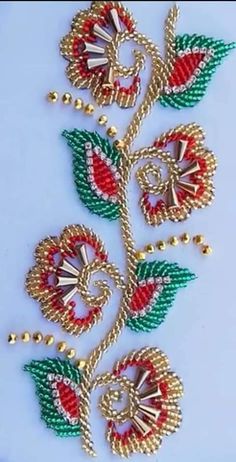 a gold and red beaded rose with green leaves on the side, sitting on a white surface